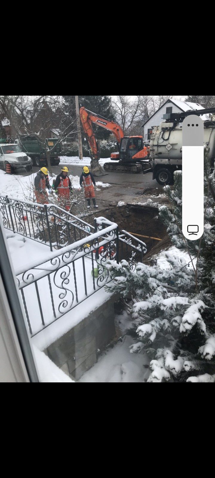 Excavator digging a front-yard sewer line in winter