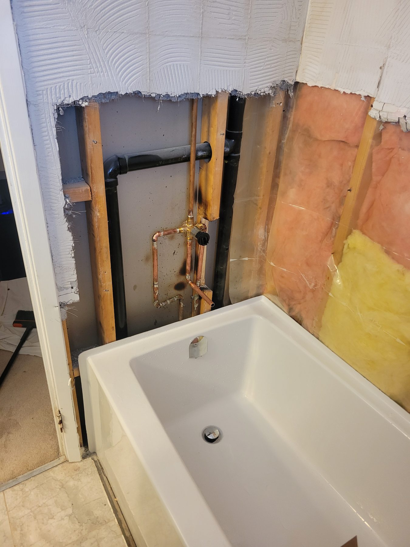 New bathtub set in place with the wall opened for rough-in plumbing